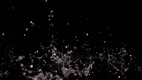 A stream of raindrops during a heavy downpour fall in slow motion against a black background