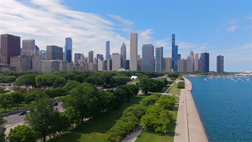 Breathtaking aerial view of Chicago Illinois skyline along lakefront showing tall skyscrapers, green park areas, coastal road and blue water of Lake Michigan