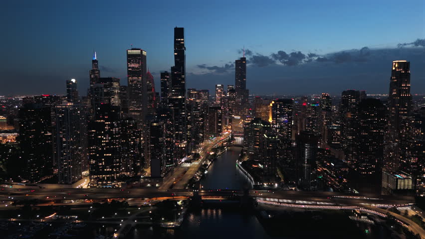 Cinematic aerial night view of Chicago skyline with illuminated skyscrapers, river reflections, glowing streets and modern downtown atmosphere, showcasing urban travel destination and city life