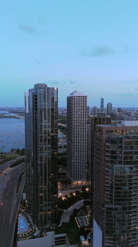 Drone perspective shows tall apartment buildings, curved lakeshore road with light traffic and distant water under cool evening sky creating layered urban depth and calm atmosphere