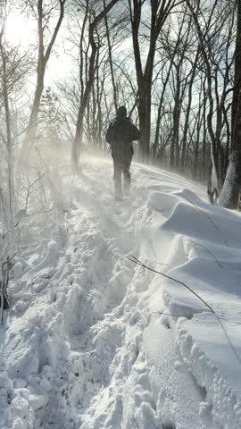 Hikers walking on a snowy mountain ridge during a heavy snowstorm with sunlight flare