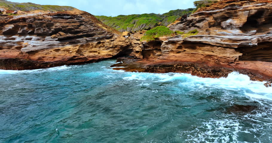 Rocky shore of Oahu, Hawaii curved by the ocean waves. Foamy waves hit the cliffs. Drone footage.