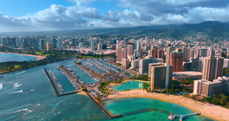 Breathtaking panorama of Honolulu, Hawaii, USA under the cloudy sky. Drone footage approaching the sandy beach of Waikiki and large yacht club.