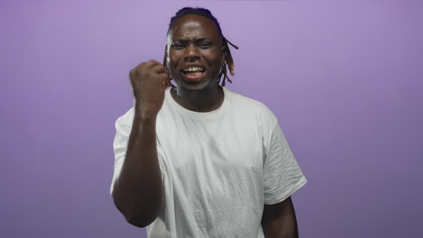 Man beckons with pinched fingers toward camera in purple studio wearing white tshirt and dreadlocks; inviting connection confidence.