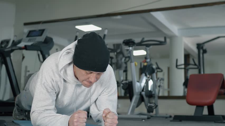 Man performing plank exercise in gym setting with workout equipment