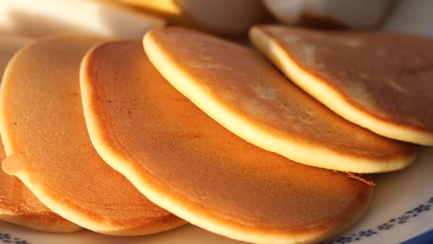 Fluffy pancakes served on a plate in warm sunlight