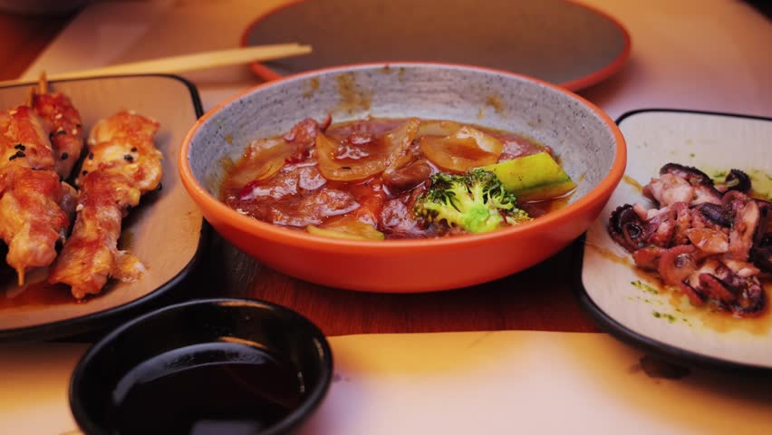 A colourful selection of Asian dishes chicken teriyaki with vegetables, grilled squid and small chicken skewers. High quality 4k footage