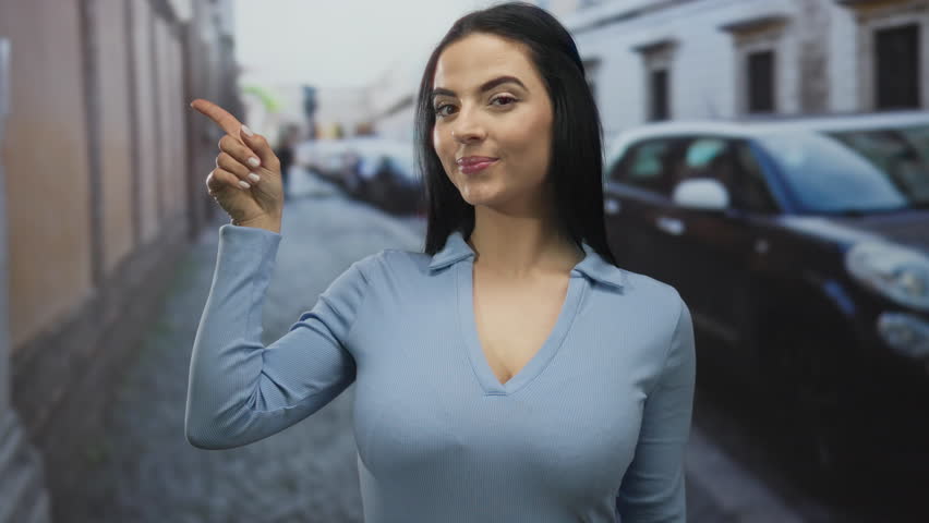 Woman in a blue shirt pointing on a street lined with cars, showcasing urban life outdoors in a captivating and lively environment during the daytime.