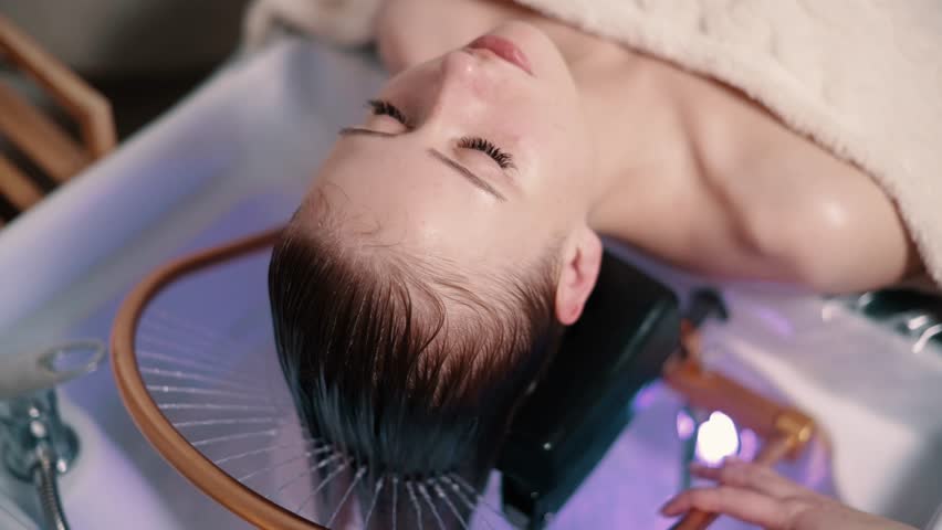 Young woman receiving a head massage during a Japanese head spa treatment with water flowing from a special hair washing tool.