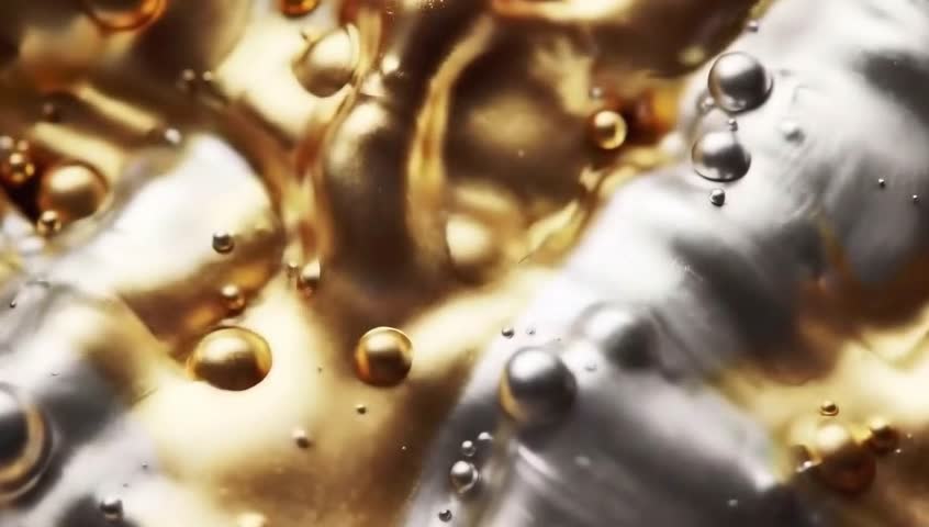 A close-up view of golden liquid with bubbles on a metallic surface, showcasing a blend of warm and cool tones, with light reflecting off the liquid and metal.