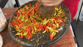 Close up hand grinding red and green chilies on a traditional stone mortar to make spicy Indonesian sambal paste. - Powered by Shutterstock - Get 15% off with code: PIKWIZARD15