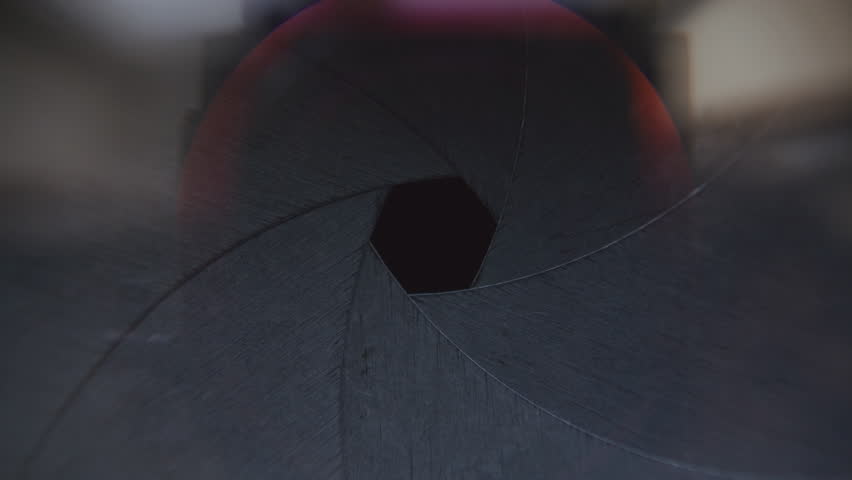 Macro view of matte black aperture blades of camera lens opening and closing, showing mechanism that controls amount of light entering camera