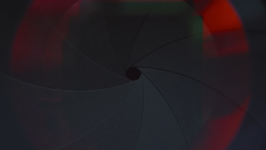 Detailed close-up view of inner aperture blades of camera lens forming wide opening with colored light reflections around edge of frame
