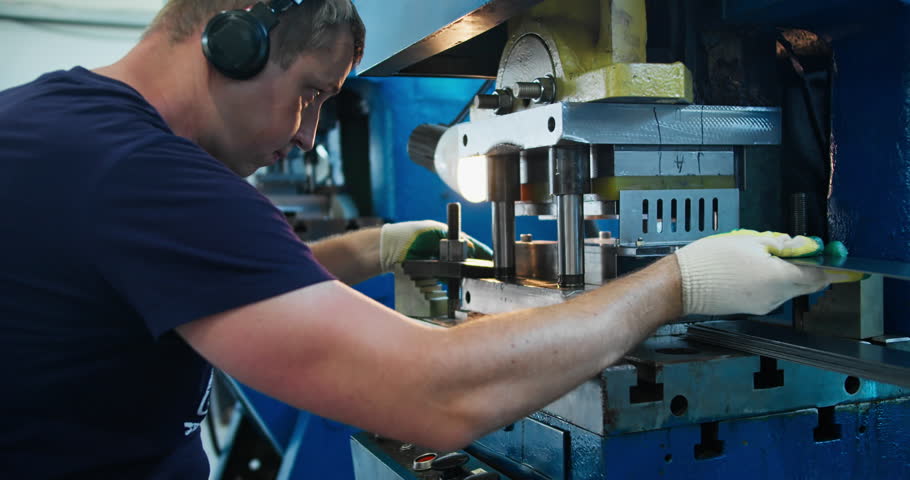 Production worker controlling metal stamping process in factory. Engineering industry and manual labor