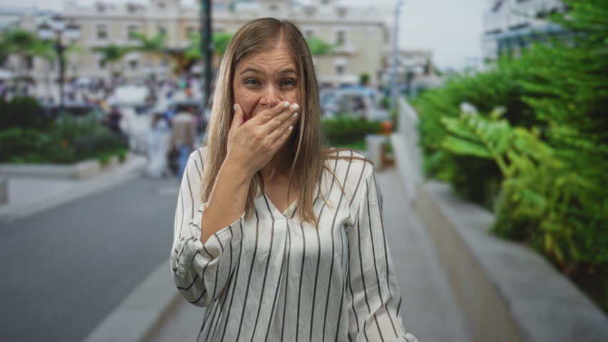 Woman raising open palms and shrugging shoulders on crowded daytime street; joy confidence optimism.