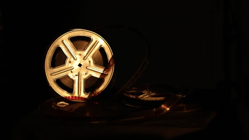 Close-up of an old-fashioned film reel, illuminated by a warm, dramatic light. Vintage cinema equipment, stored in the dark, evokes nostalgia and the magic of classic filmmaking.