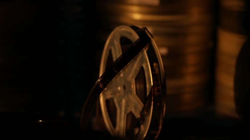 Close-up of an old-fashioned film reel, illuminated by a warm, dramatic light. Vintage cinema equipment, stored in the dark, evokes nostalgia and the magic of classic filmmaking.
