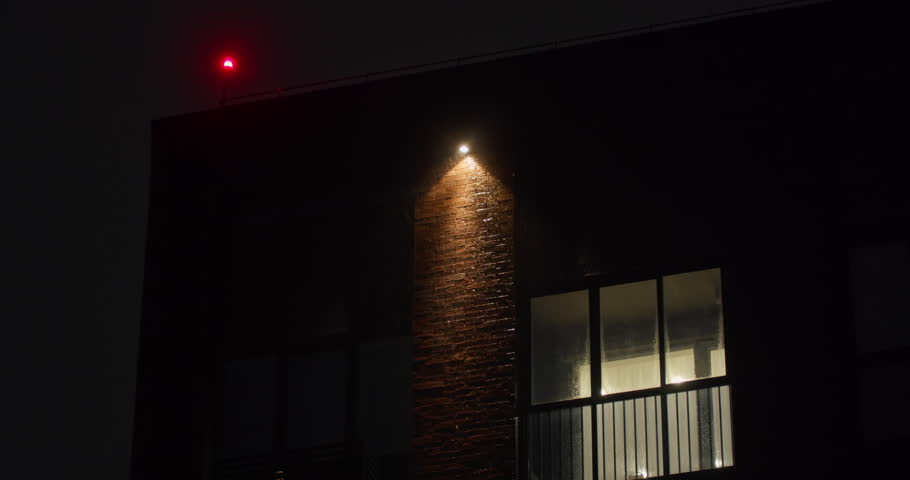 Heavy rain falling at night under street light with visible raindrops and illuminated building. Severe weather conditions