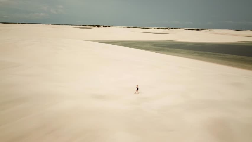 Lencois Maranhenses National Park full of dunes and lagoons. Girl running to get to Rota Lagoa Azul, Maranhao, Brazil. High quality 4k footage
