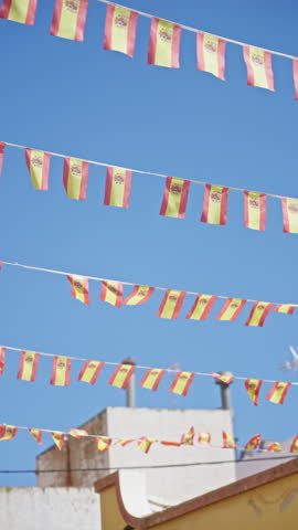 Spanish flags flutter in the sunny outdoors against a clear blue sky, showcasing the vibrant national colors of spain in a festive environment.