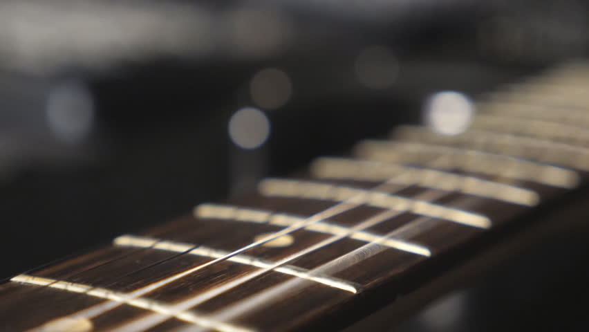 Dolly shot of chords being strummed and vibrating during playing. Close up of trembling guitar strings against fret. Beautiful background with wooden texture. Music performance. Slow motion