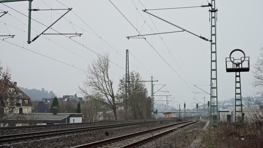 Quiet Train Corridor, Desolate Rural Track Scene, Overcast Countryside Railway With Signals And Distant Horizon, Gray Sky Over Silent Rural Train Tracks With Power Lines And Leafless Trees