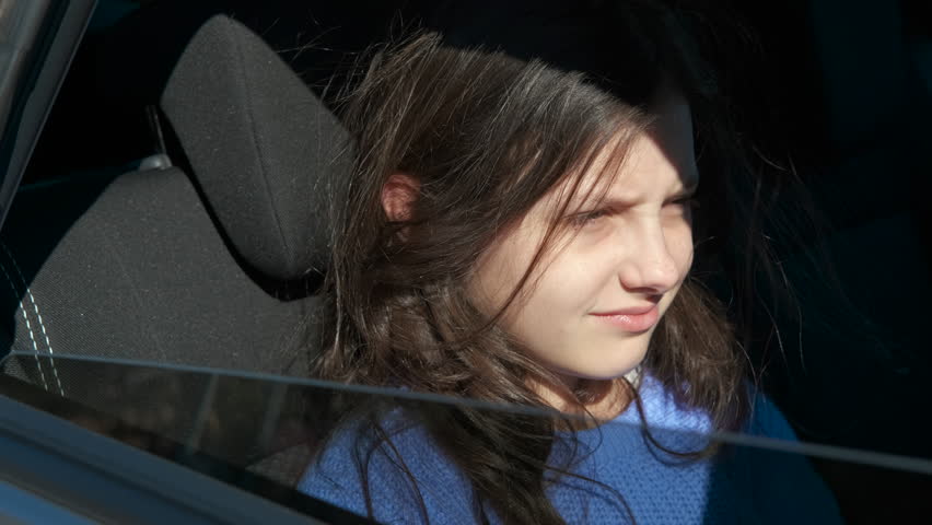 Sleepy young girl yawning in car during trip. Tired young girl in a blue sweater yawning while sitting in the passenger seat of a moving car, struggling to stay awake on a sunny day during a road trip