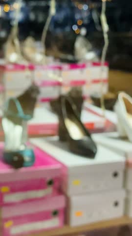 blurred shoe display in store with stacked shoeboxes and heels on shelves, soft retail lighting and festive string lights, sales associate Taken on mobile device.