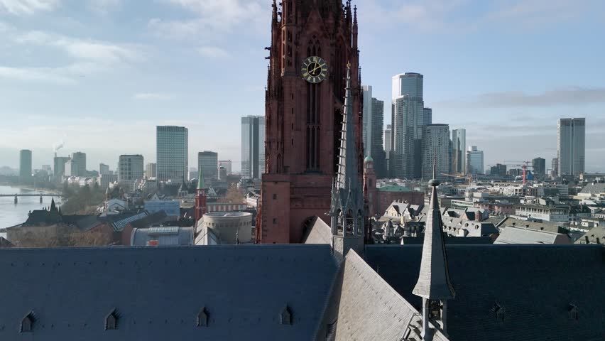 Aerial drone footage of Frankfurt Cathedral featuring a close view of the clock tower and moving clock hands. Captured on a clear, sunny winter day at midday, highlighting historic architecture against the bright sky.