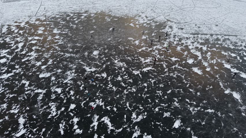 Aerial view shows people ice fishing on a frozen river. Snow covers the ice surface. The video documents activity, showcasing a winter landscape - Plzen, Czech - Jan,11,2026