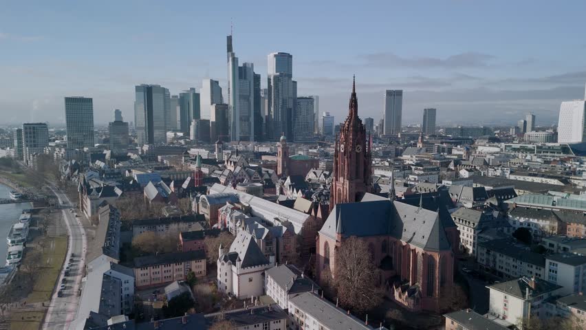 Aerial drone footage of Frankfurt Cathedral featuring a close view of the clock tower and moving clock hands. Captured on a clear, sunny winter day at midday, highlighting historic architecture against the bright sky.