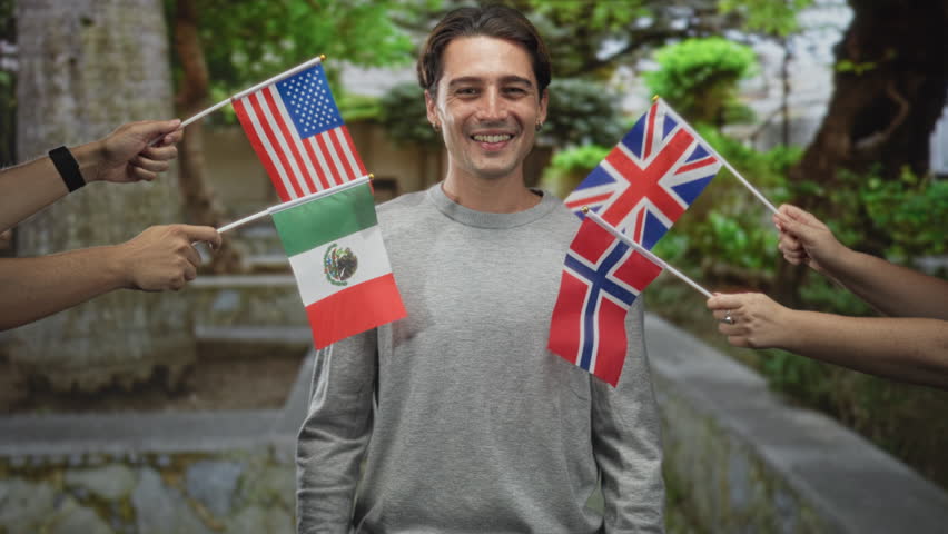 Man holding three small national flags from usa mexico norway and giving thumbs up in forest pathway, smiling broadly; unity celebration joy.