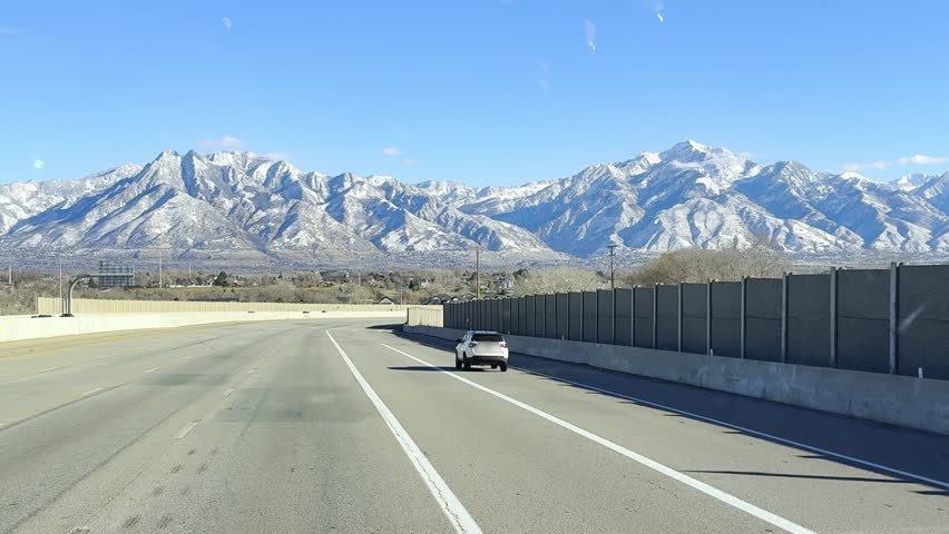 View from a semi-truck cabin driving on a highway in Salt Lake City. Majestic snow-capped Utah mountains under a bright morning sun. Passenger cars and traffic on the road. Professional logistics.