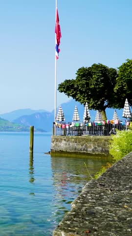 Serene lakeside scene, Calm lakeside promenade with trees and distant mountains under clear sky