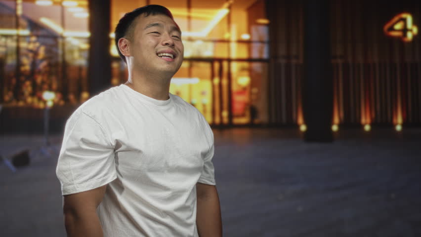 Man in white shirt smiles with bare arms under glowing streetlights on city street at night; happiness confidence warmth.