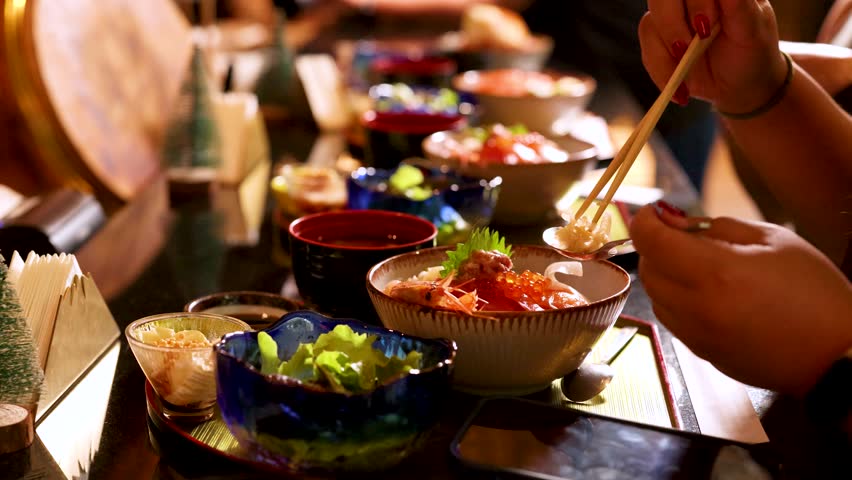 Close-up of a person using chopsticks to eat a fresh seafood rice bowl in restaurant