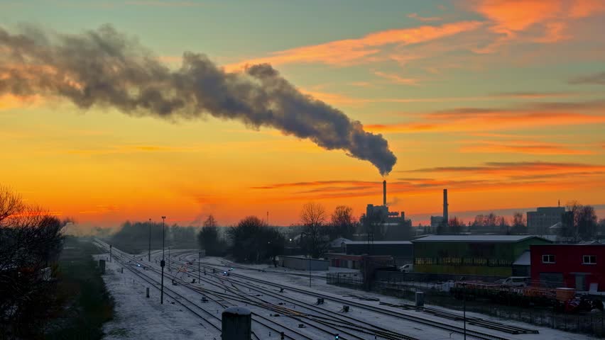 Industrial area at sunrise sunset factory chimney emitting a large plume of smoke orange skyline