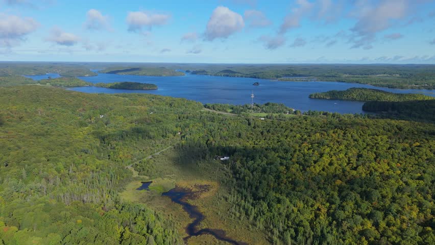 Drone aerial over Lake Vernon near Huntsville, Muskoka, Ontario, showing blue water, forested islands and cottage country shoreline under a clear sky.