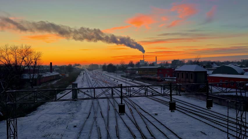 Sunset view of snowy train tracks and smoke over industrial area