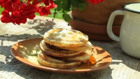 Stack of pancakes with pouring maple syrup on garden table.