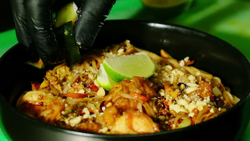 Cook finishes aroma pad thai noodles with prawns and peanuts. Chef places warm zucchini chunks before pressing lime wedge over dish top