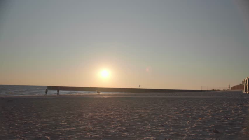 EVANSTON, UNITED STATES – JANUARY 12, 2026: People walking with a dog along the sandy shoreline at Lake Michigan during a golden sunset.