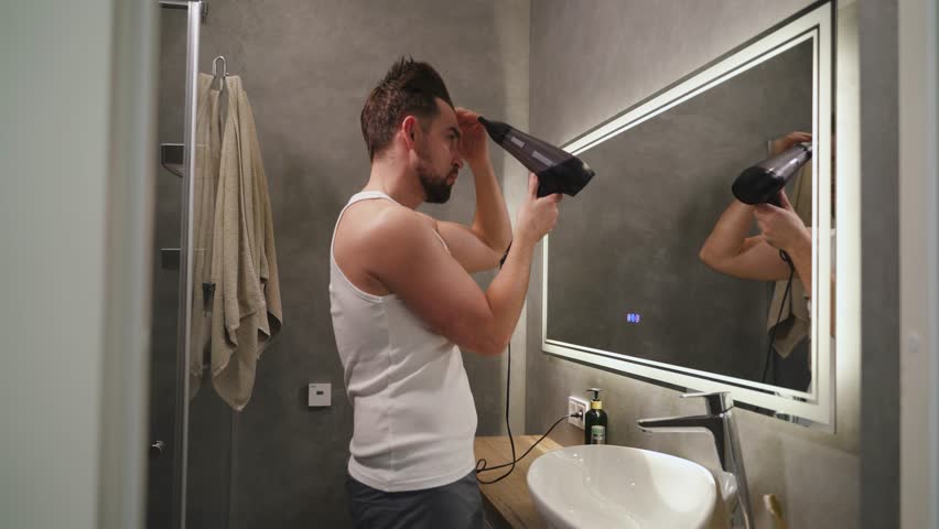 Man Drying Hair with Blow Dryer in Modern Bathroom