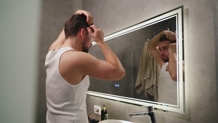 Man combing his hair while looking into a mirror in a modern bathroom