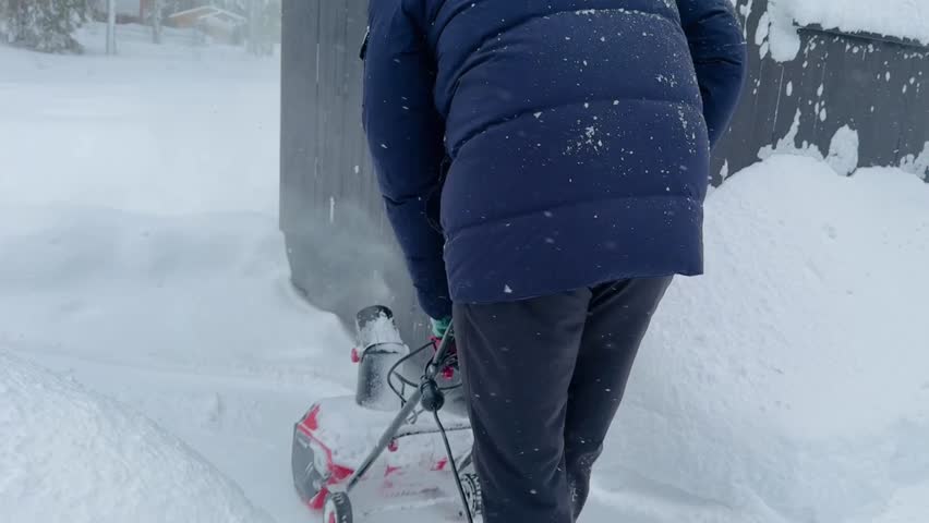 man clearing snow in countryside using electric snow blower. Snowing weather conditions
