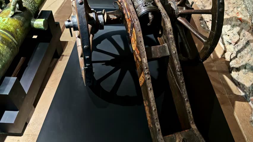 Historic cannons and wheeled artillery on display at Wawel Royal Castle ramparts, Krakow, Poland, beside brick and stone fortress walls in bright daylight.