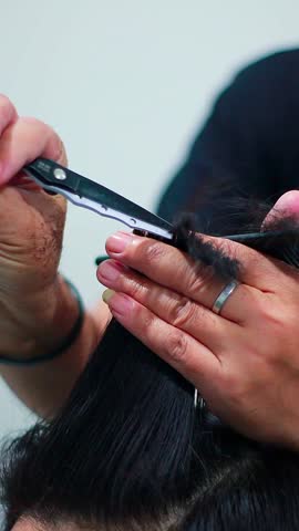 Close-up of a barber’s hand cutting a customer’s hair with scissors inside a barbershop.