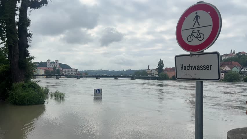 Flooding in Passau, Germany, as the Inn River reaches high water levels in June 2024. Submerged riverside path with official flood warning sign, documenting an active urban flood situation.