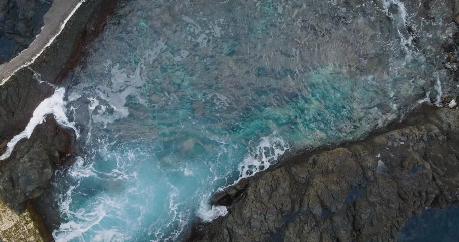 Drone shot capturing the turquoise waters of a natural ocean pool surrounded by dark volcanic rock formations on Tenerife