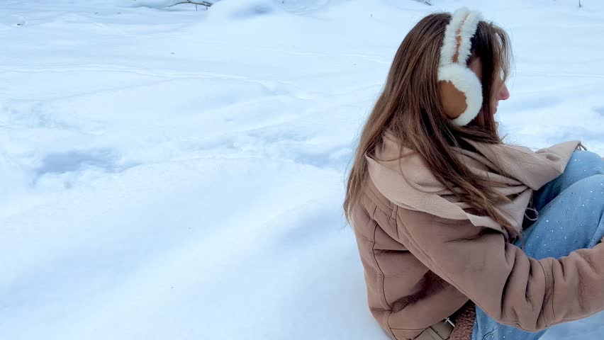 Teenage girl making a snow angel in a winter forest. Playful winter activity, childhood joy, freedom and authentic outdoor lifestyle moment.